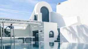 A modern pool area with a clear view of the pool, a pergola, and a building with a distinctive arched door. - Opera Mansion (Santorini)