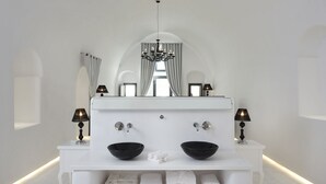 A modern bathroom with a white vanity, two black bowls, a chandelier, and a large mirror. - Opera Mansion (Santorini)