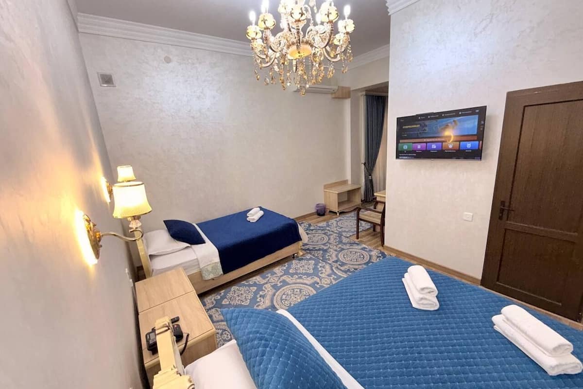 Habitación de hotel con una cama grande, una cama más pequeña, un escritorio con lámpara, un televisor y una puerta.
