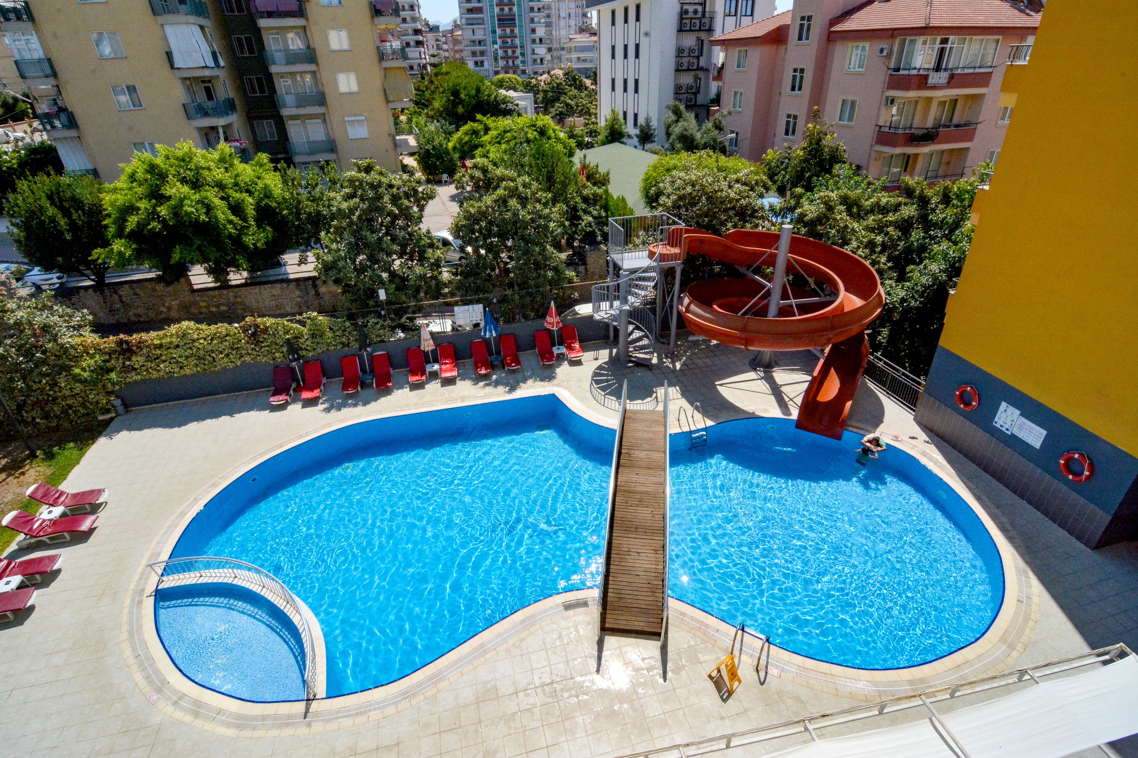 A swimming pool with a slide, surrounded by lounge chairs and a small deck area.