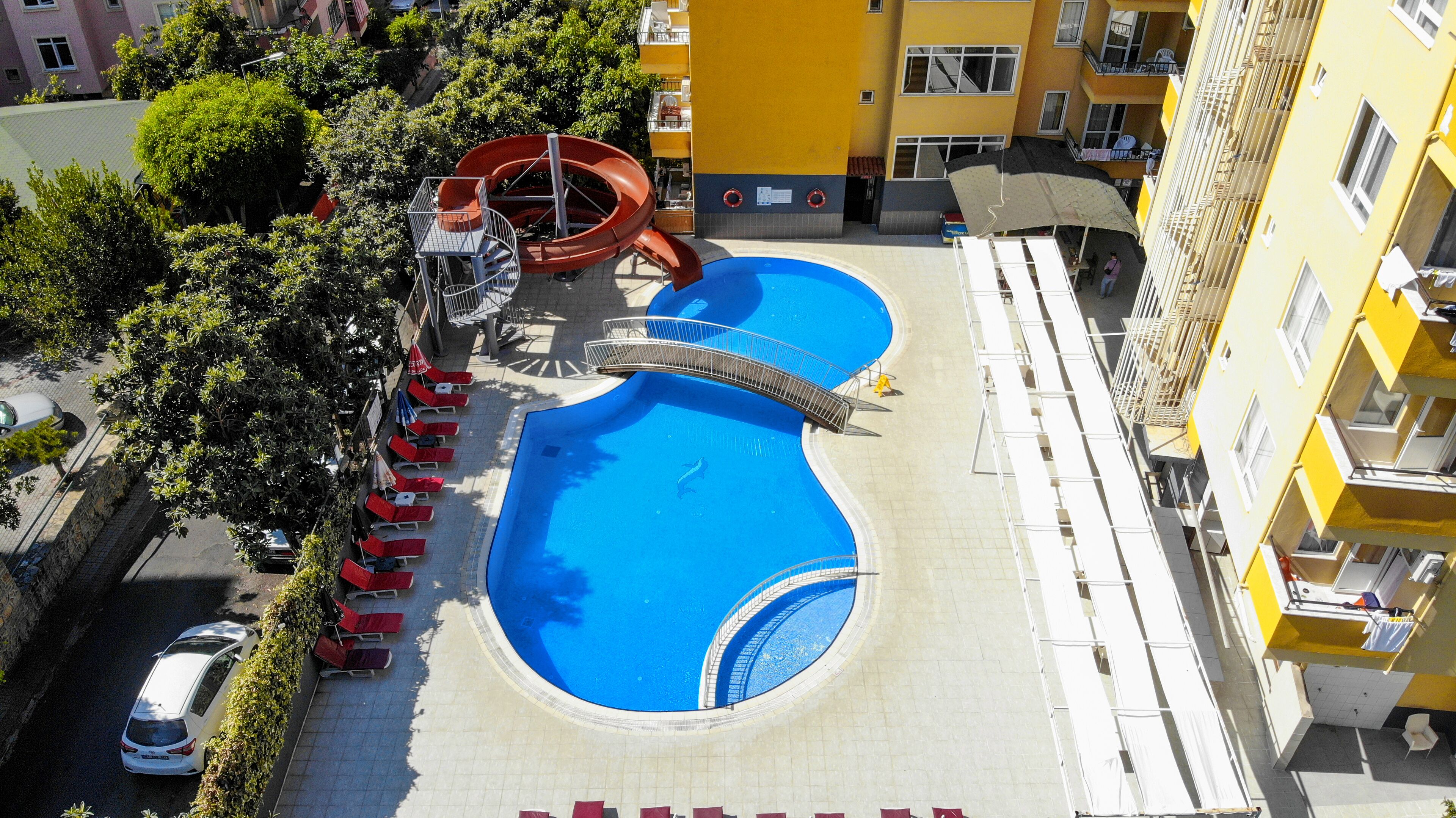A swimming pool with a slide, surrounded by lounge chairs and a bridge.