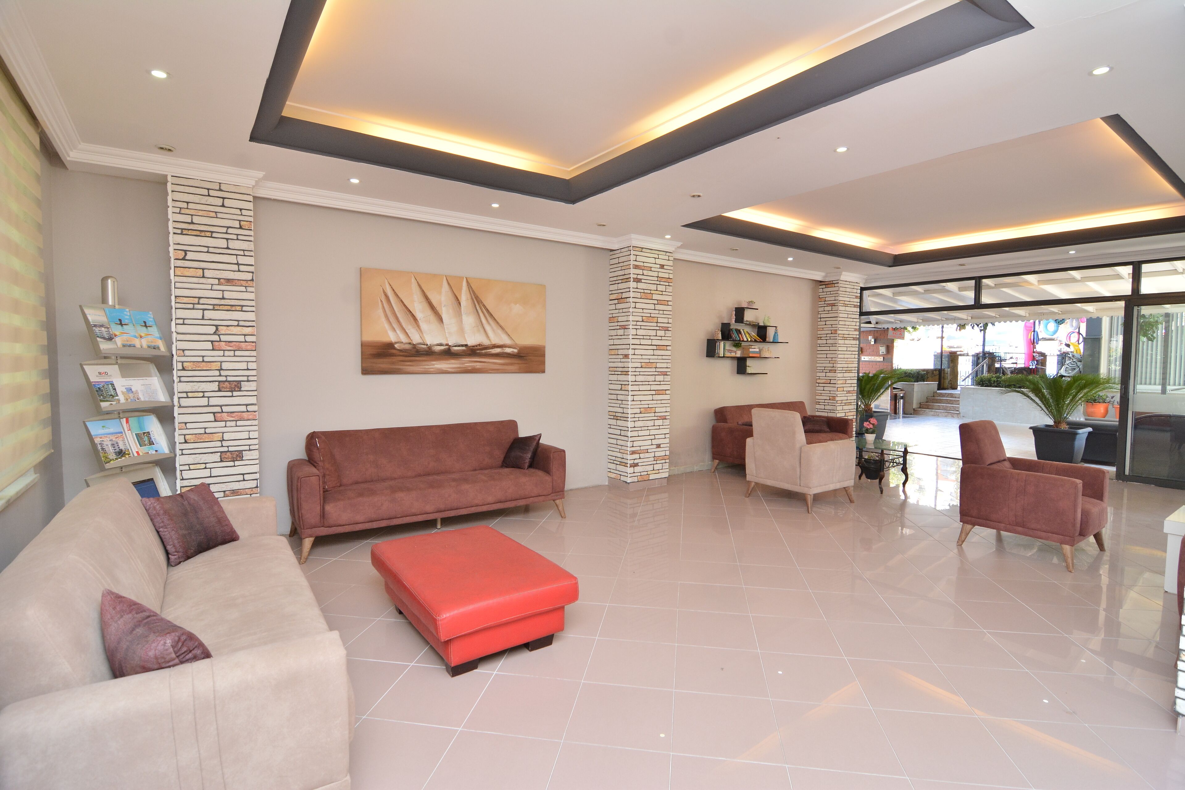 A spacious lobby with a beige sofa, a red ottoman, and a bookshelf.