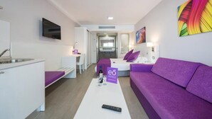 A modern hotel room with a kitchenette, a purple sofa, a bed with a purple headboard, and a TV mounted on the wall. - eó Corona Cedral (Mogan)