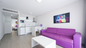 A modern living room with a purple sofa, a white coffee table, and a kitchen area in the background. - eó Corona Cedral (Mogan)