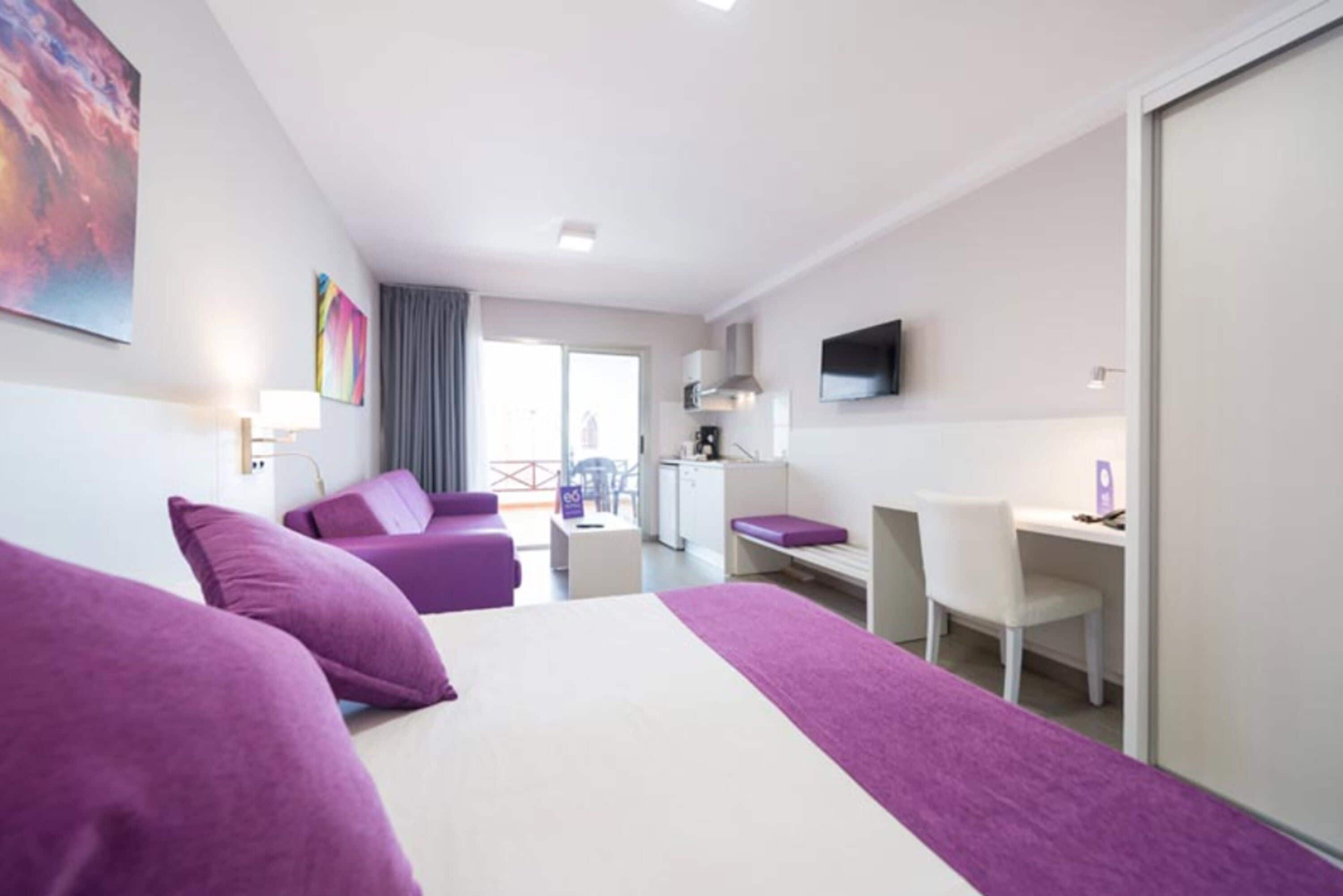 A hotel room with two beds, a desk, a chair, a TV, and a balcony with a view.