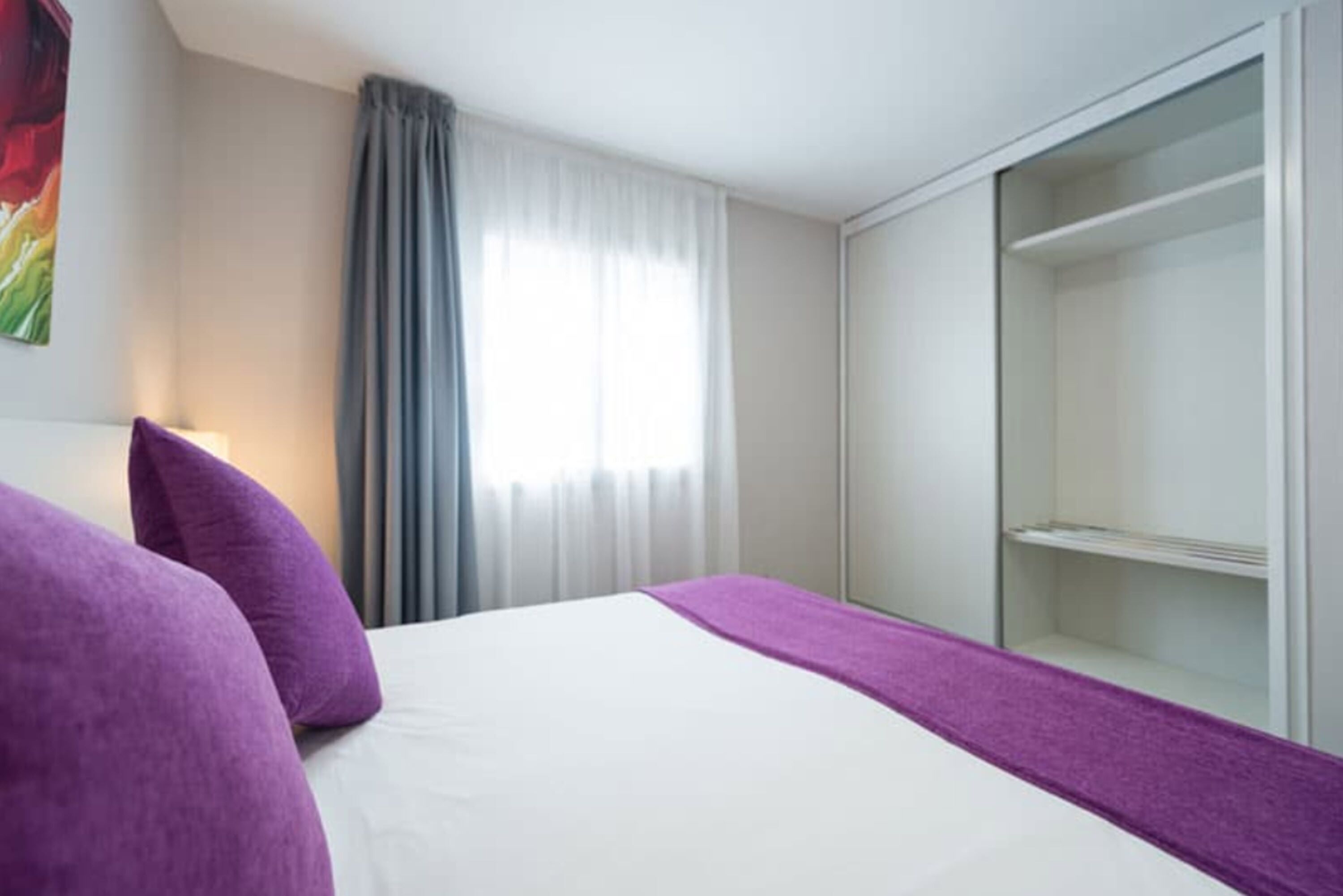 A hotel room with a bed, a wardrobe, and a window with curtains.