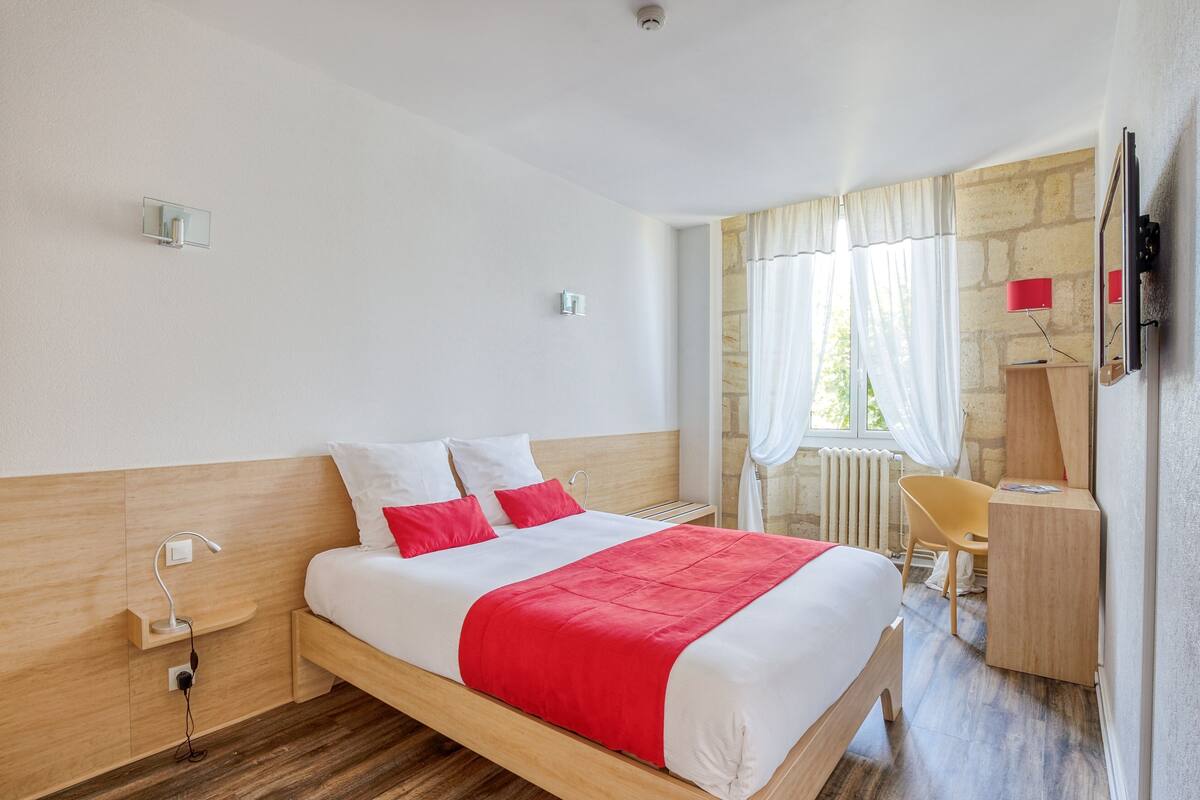 Une chambre d’hôtel équipée d’un lit, d’une table de chevet, d’une lampe, d’une chaise, d’un bureau et d’un téléviseur fixé au mur.