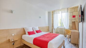A hotel room with a bed, bedside table, lamp, chair, desk, and a TV mounted on the wall.