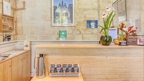 Uma receção com um quadro de um edifício, uma máquina de café e um vaso com flores.