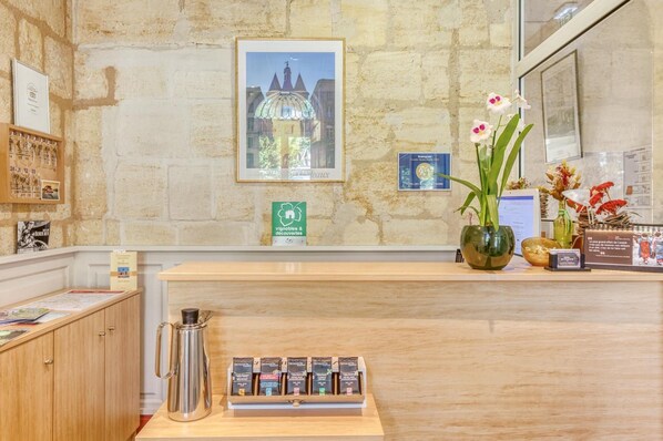 A reception desk with a framed picture of a building, a coffee machine, and a vase with flowers. - Logis Hôtel des Voyageurs (Bordeaux)