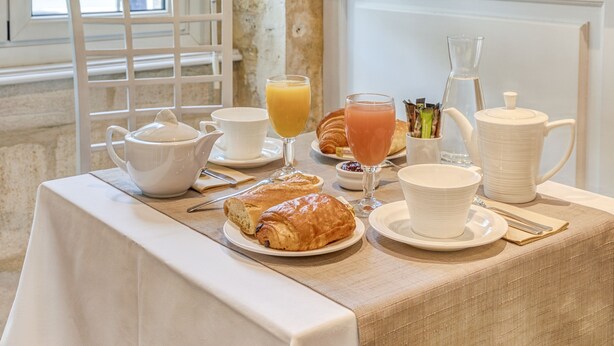 Uma mesa de café da manhã com croissants, suco, café e chá.