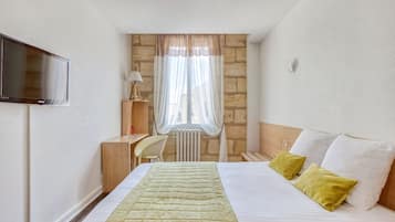 Una habitación de hotel con cama, televisión, escritorio y ventana con cortinas.