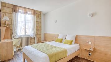 Habitación de hotel con cama de madera, un escritorio, una silla, un radiador y una ventana con cortinas.