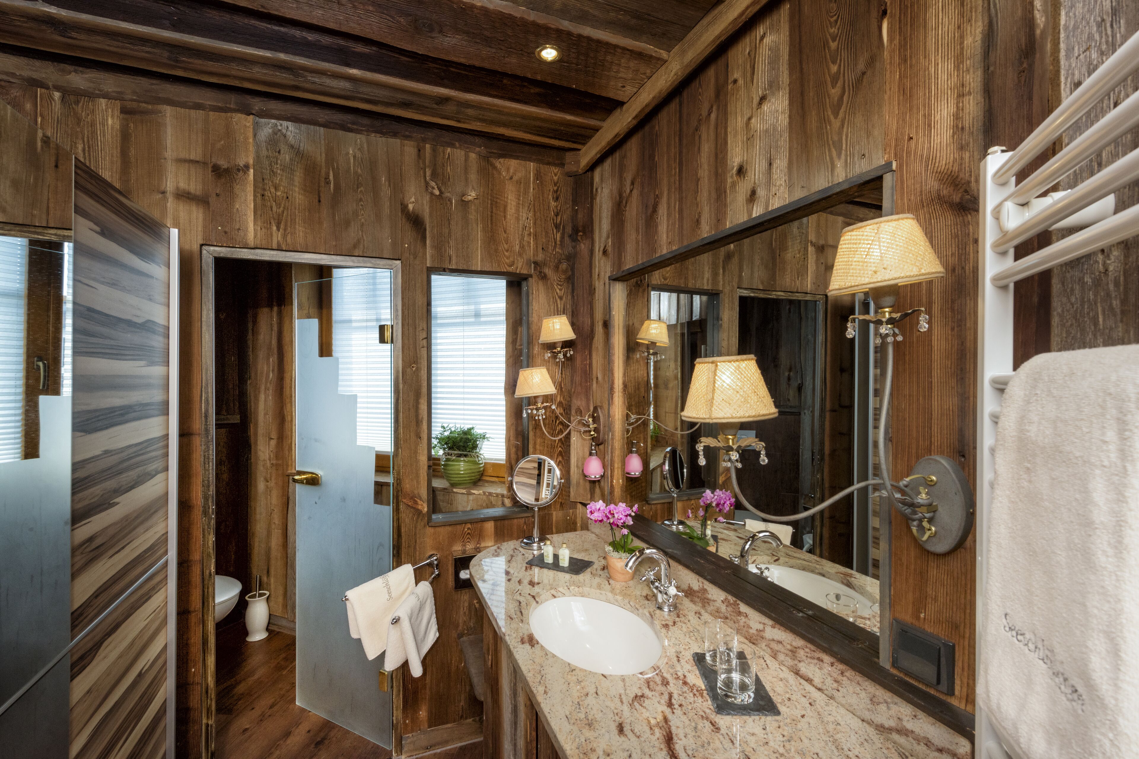 A bathroom with wooden walls, a large mirror, two sinks, and a toilet.