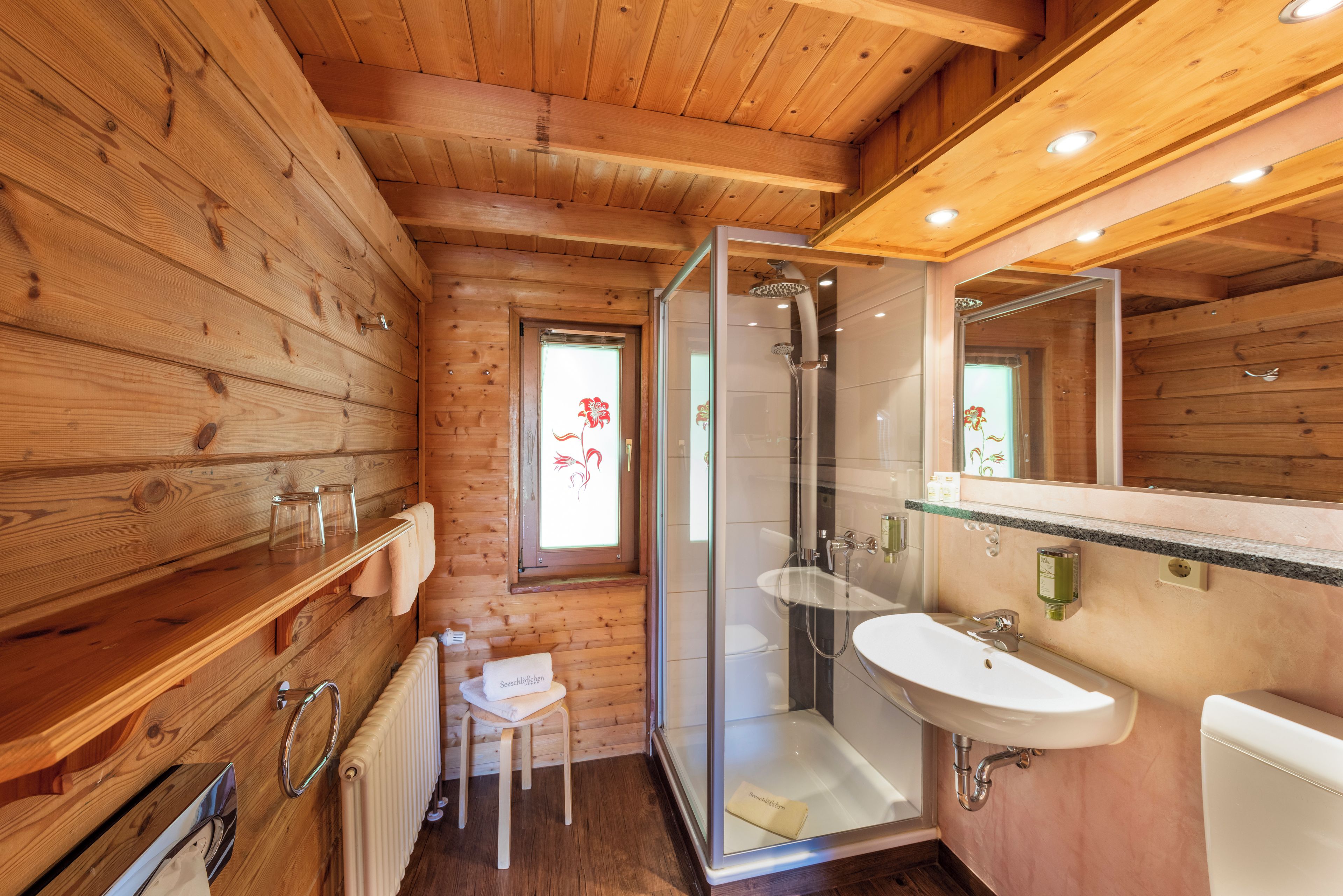 A wooden cabin bathroom with a glass shower enclosure, a sink, and a toilet.