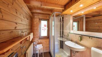 A wooden cabin bathroom with a glass shower enclosure, a sink, and a toilet.