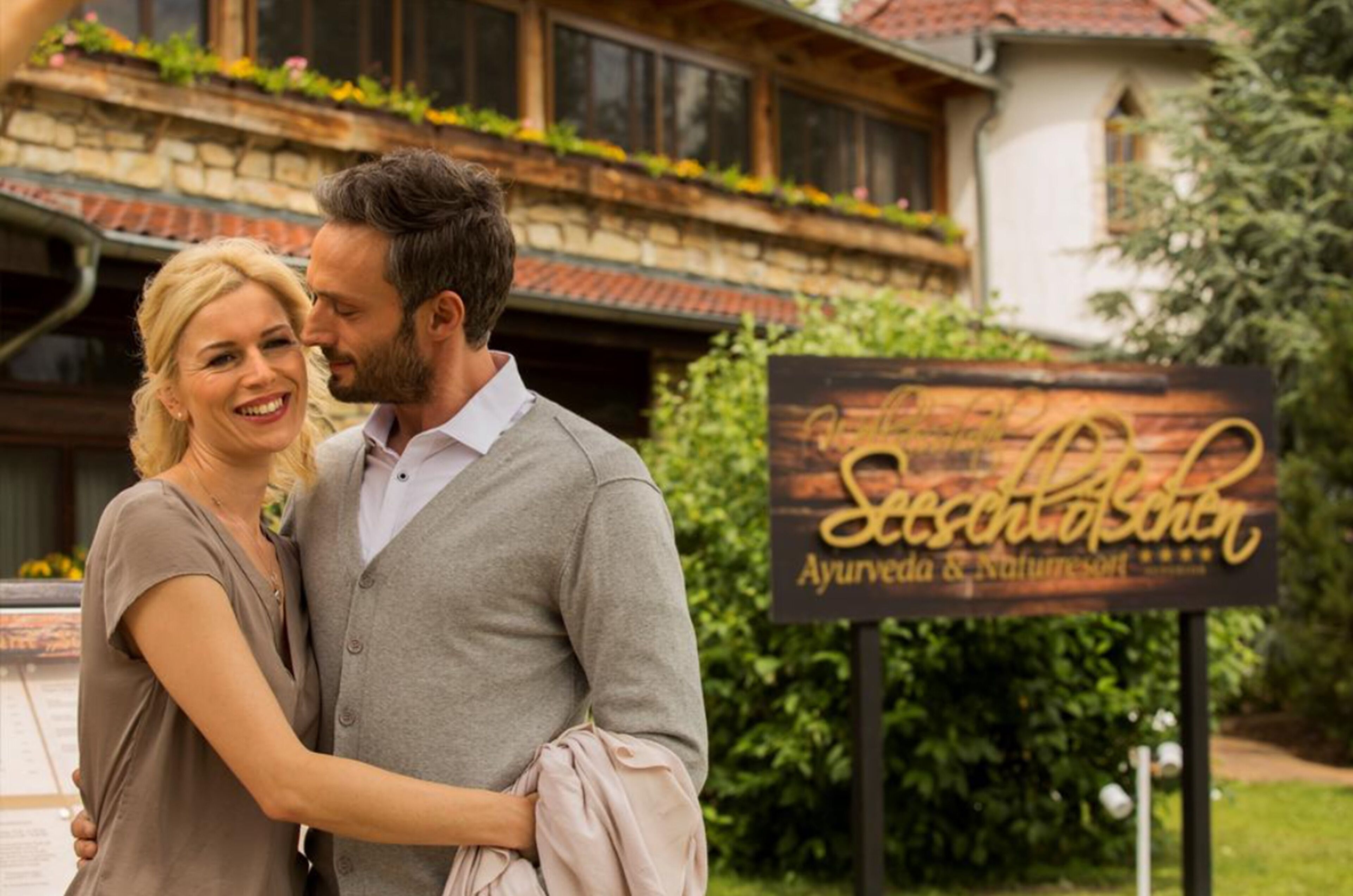Un couple s’embrasse devant une enseigne indiquant « Schloss Aschaffenburg Ayurveda & Naturheilkunde ».