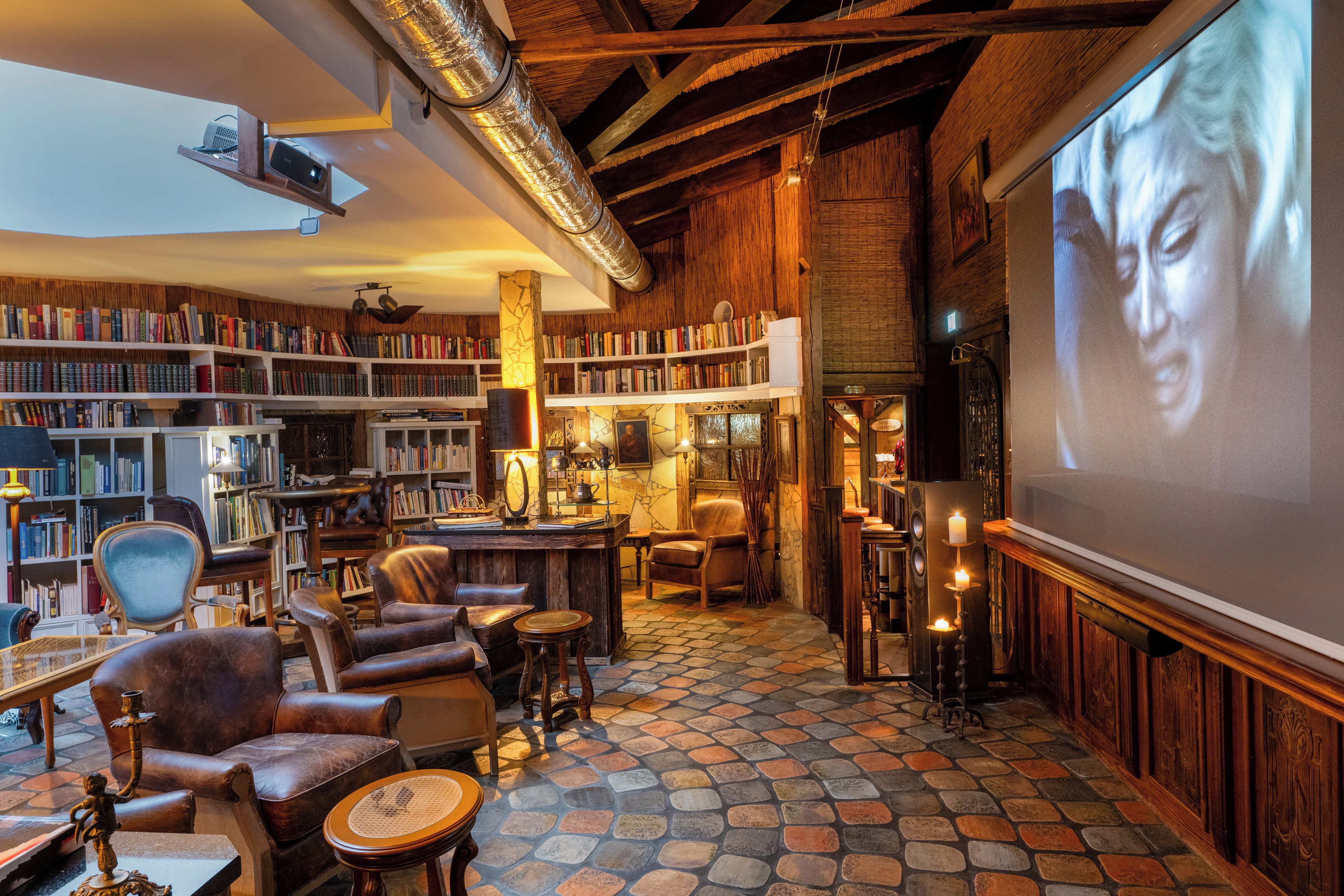 A cozy library with bookshelves, leather chairs, a fireplace, and a large screen for presentations.