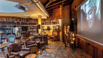 A cozy library with bookshelves, leather chairs, a fireplace, and a large screen for presentations.