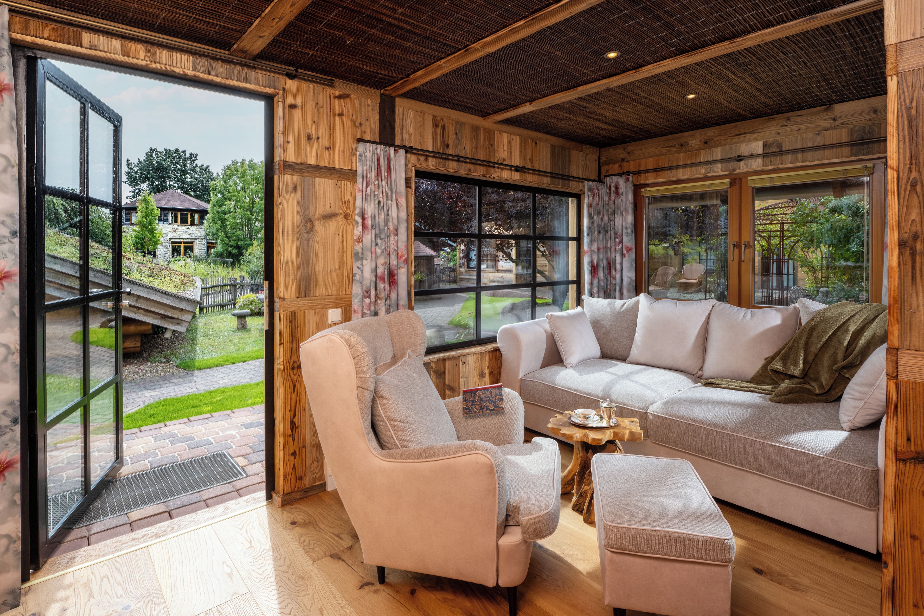 A cozy living room with a sectional sofa, a chair, and a coffee table. Large windows offer a view of the outdoors.