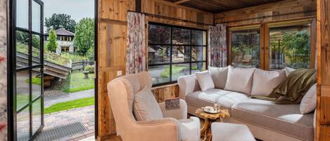 A cozy living room with a sectional sofa, a chair, and a coffee table. Large windows offer a view of the outdoors.
