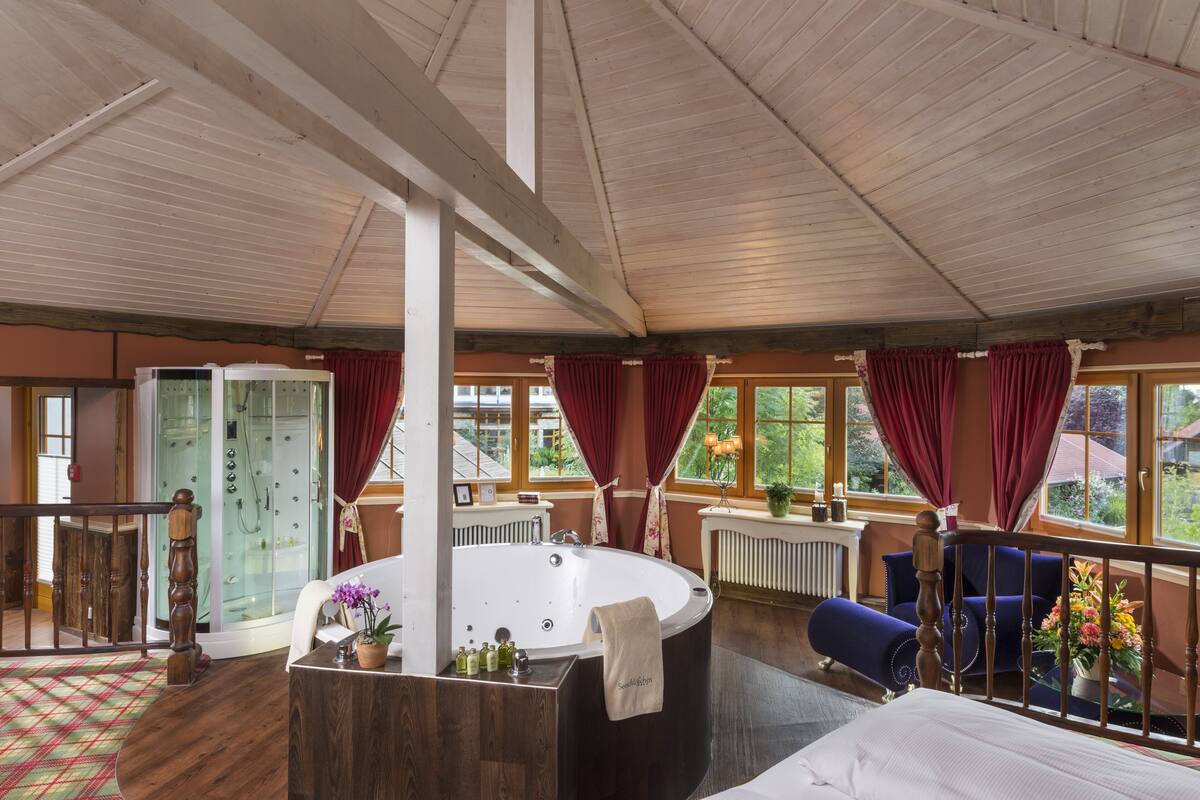 Ein geräumiges Zimmer mit einer großen Badewanne, einer Dusche und einem Balkon mit roten Vorhängen.