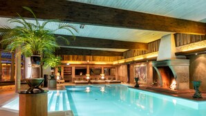 Uma grande piscina coberta com vigas de madeira, lareira e áreas de estar.