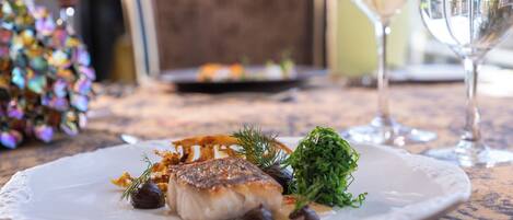 A plate of food with a white plate, a glass of white wine, and a chair in the background.