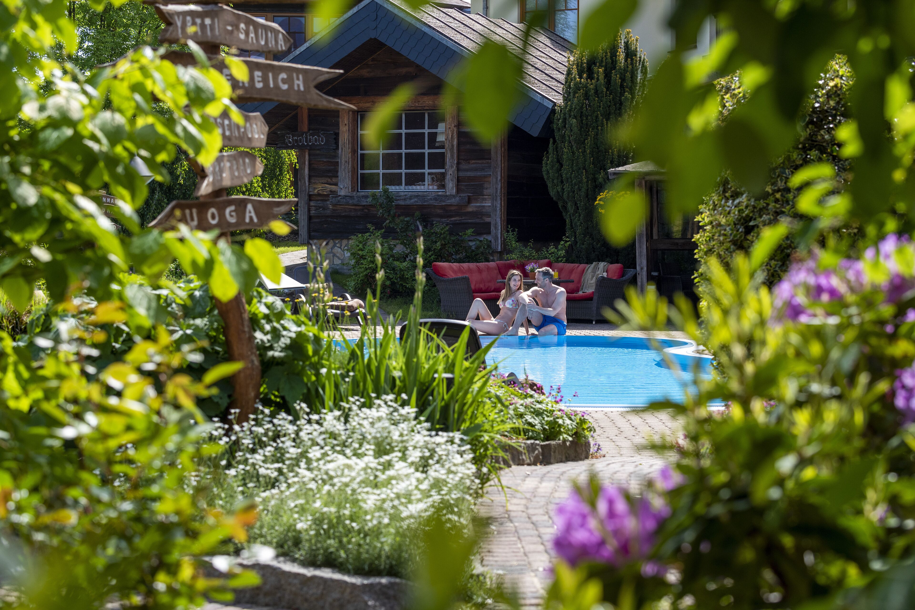 Una cabaña de madera con piscina, rodeada de abundante vegetación y un sofá rojo.