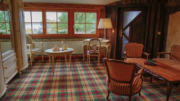 Une pièce dotée d’un tapis à carreaux, de meubles en bois, d’une table avec des chaises, d’un radiateur et de grandes fenêtres donnant sur un paysage verdoyant.