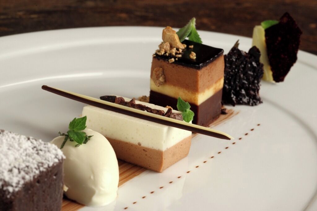 Un plato de postres con distintos tipos de pasteles y dulces, incluyendo un pastel con capas y nueces y un trozo de chocolate.