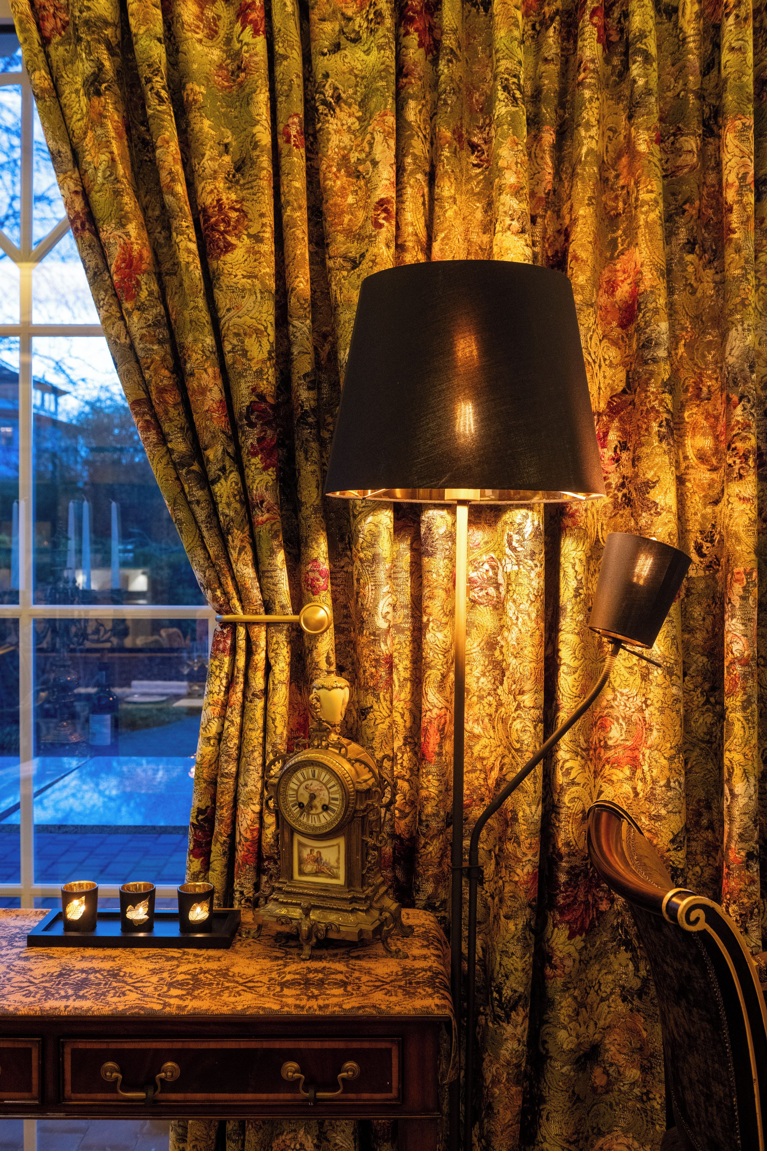 A room with a desk, a lamp, and curtains with a floral pattern.