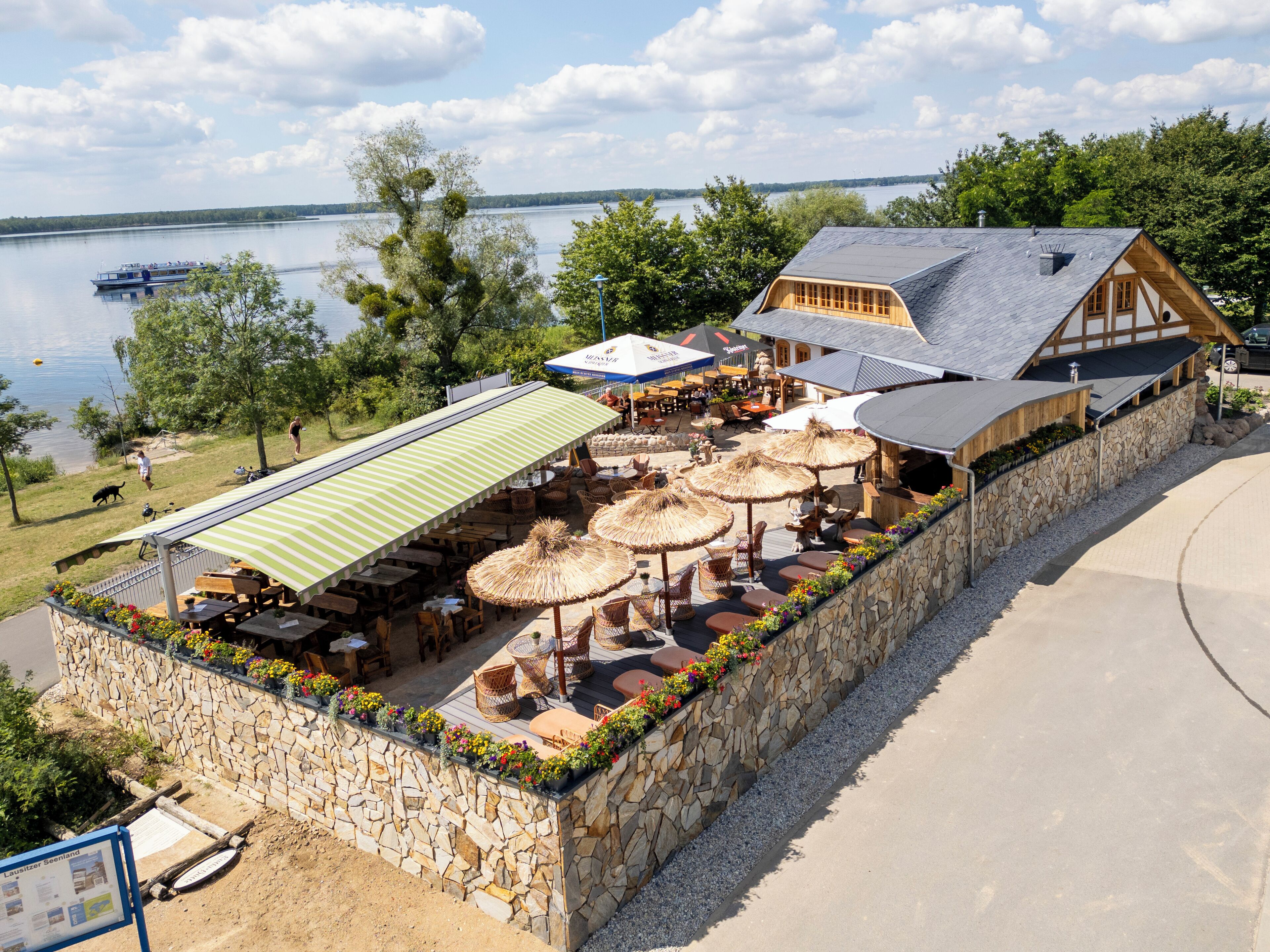 Un restaurante junto al lago con terraza, paredes de piedra y vistas al lago.