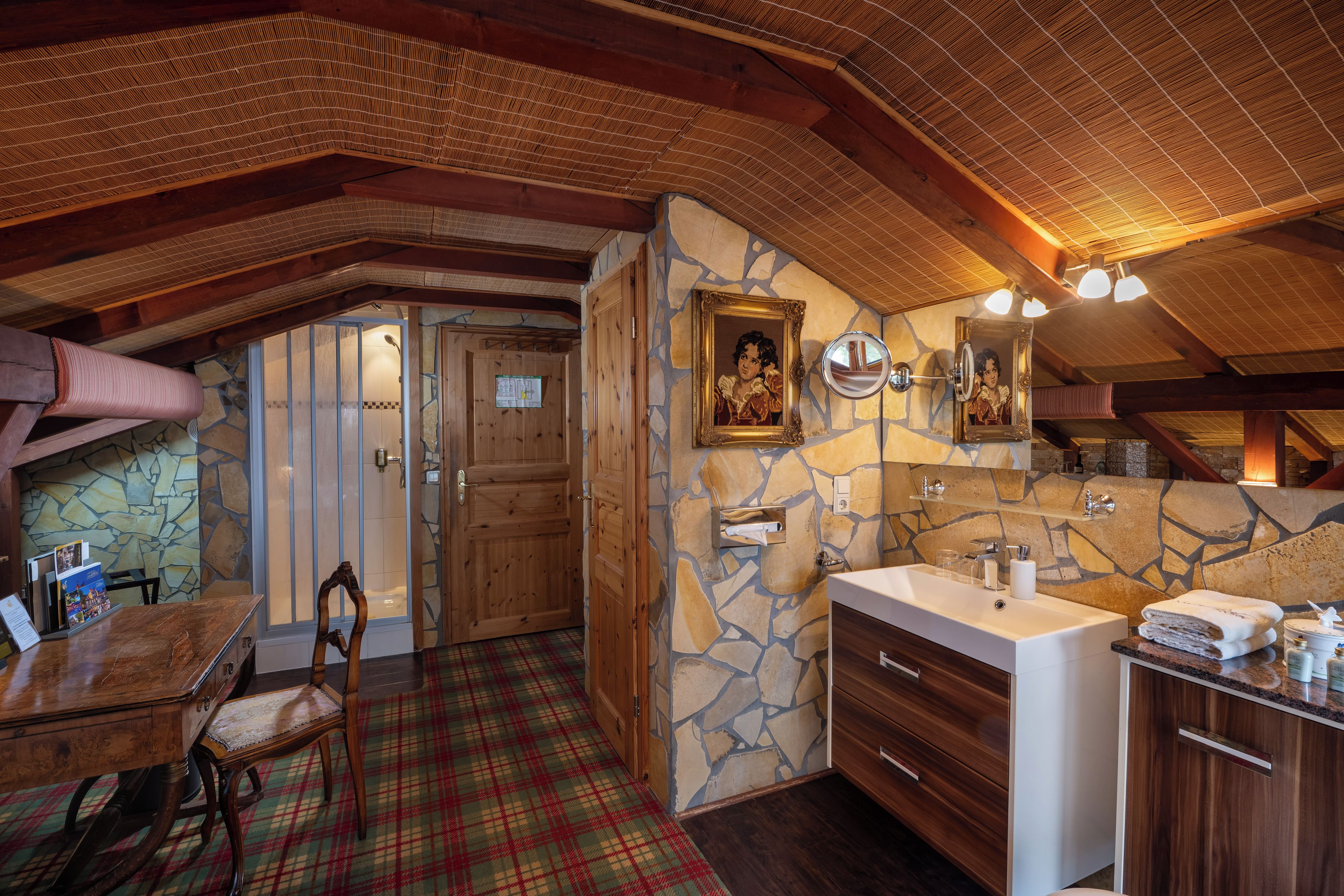 Un baño rústico con pared de piedra, techo de madera y un espejo grande.