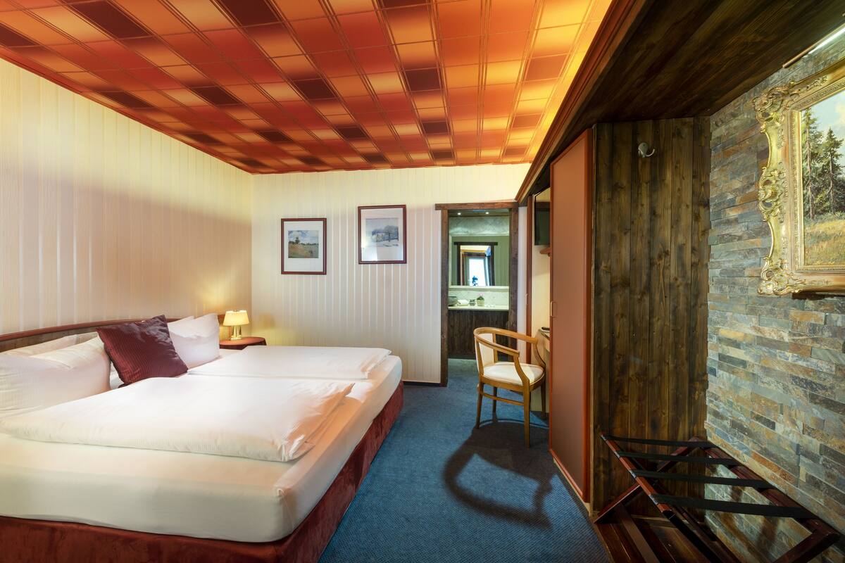 Ein Hotelzimmer mit einem großen Bett, einem Sessel, einem Schreibtisch und einem durch eine offene Tür einsehbaren Badezimmer.