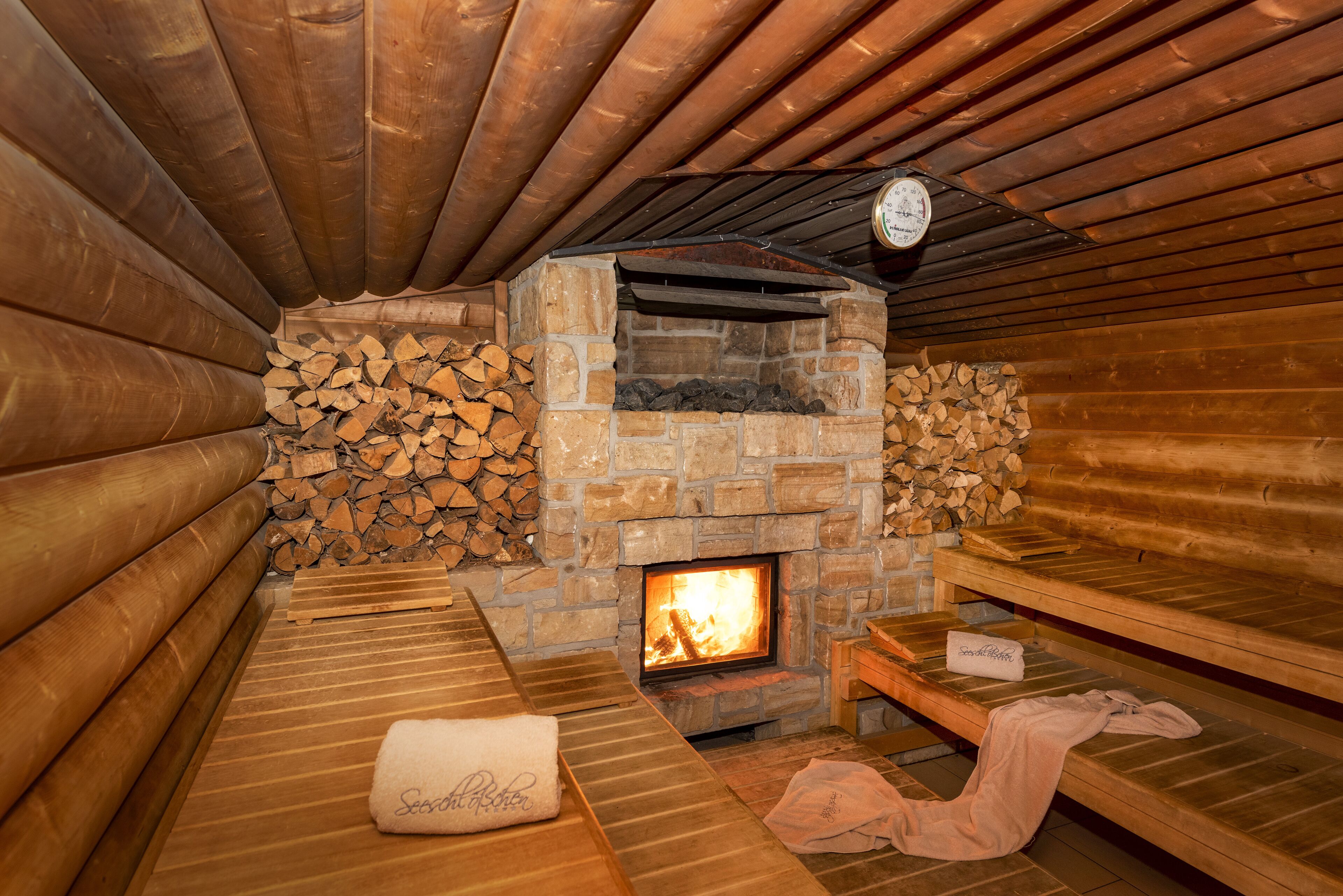 A sauna with wooden benches, a stone wall, and a visible fire.