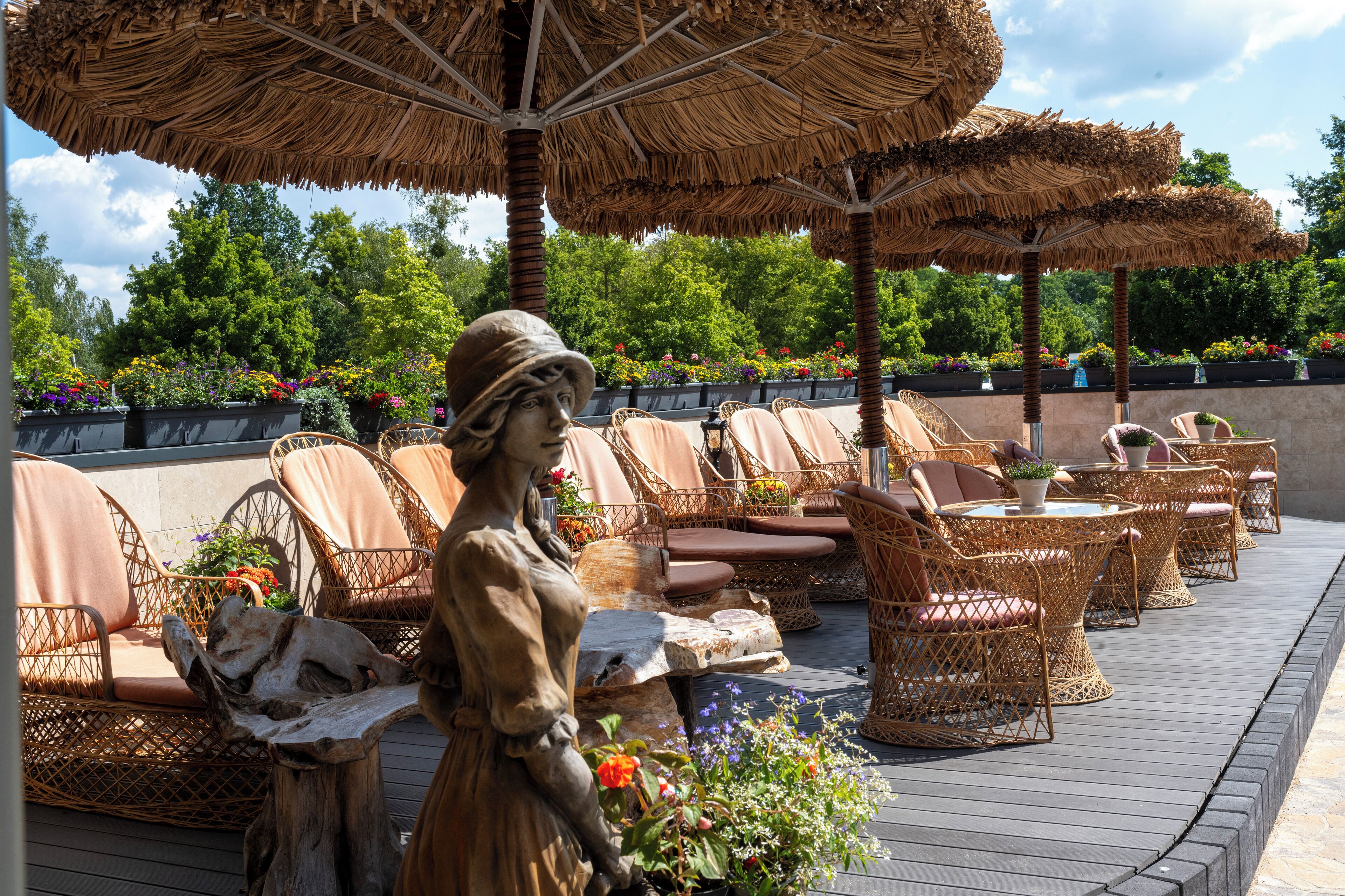 A patio area with wicker furniture, thatched umbrellas, and a statue.