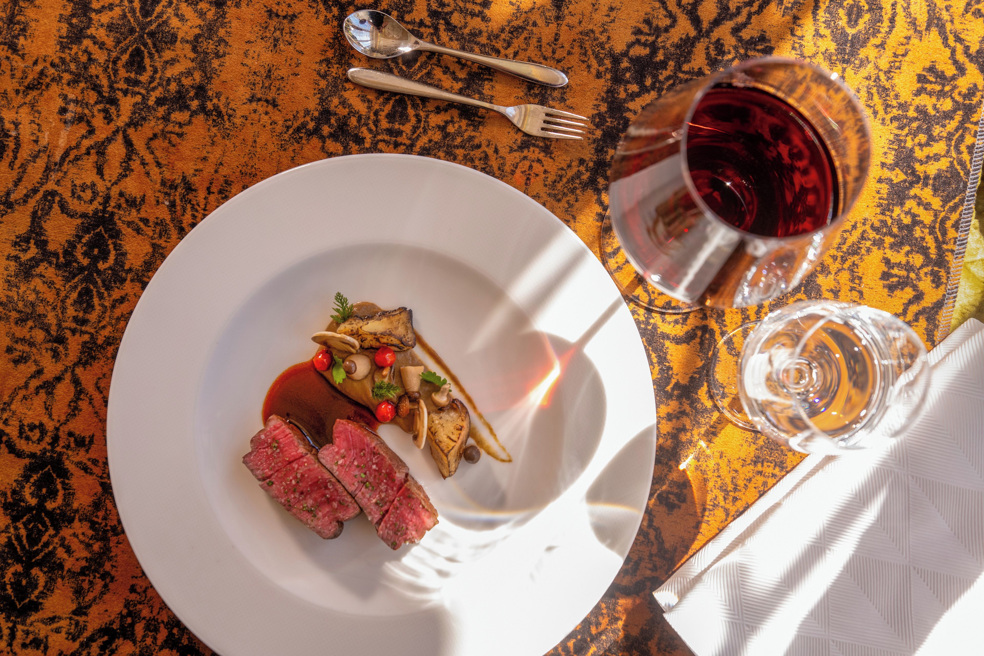 Une table à manger avec une assiette de nourriture, un verre de vin rouge et des couverts.