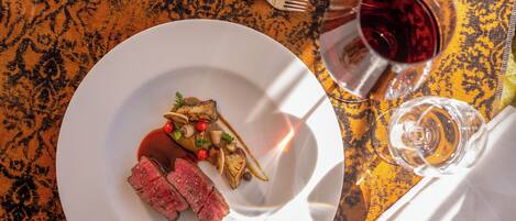 Une table à manger avec une assiette de nourriture, un verre de vin rouge et des couverts.
