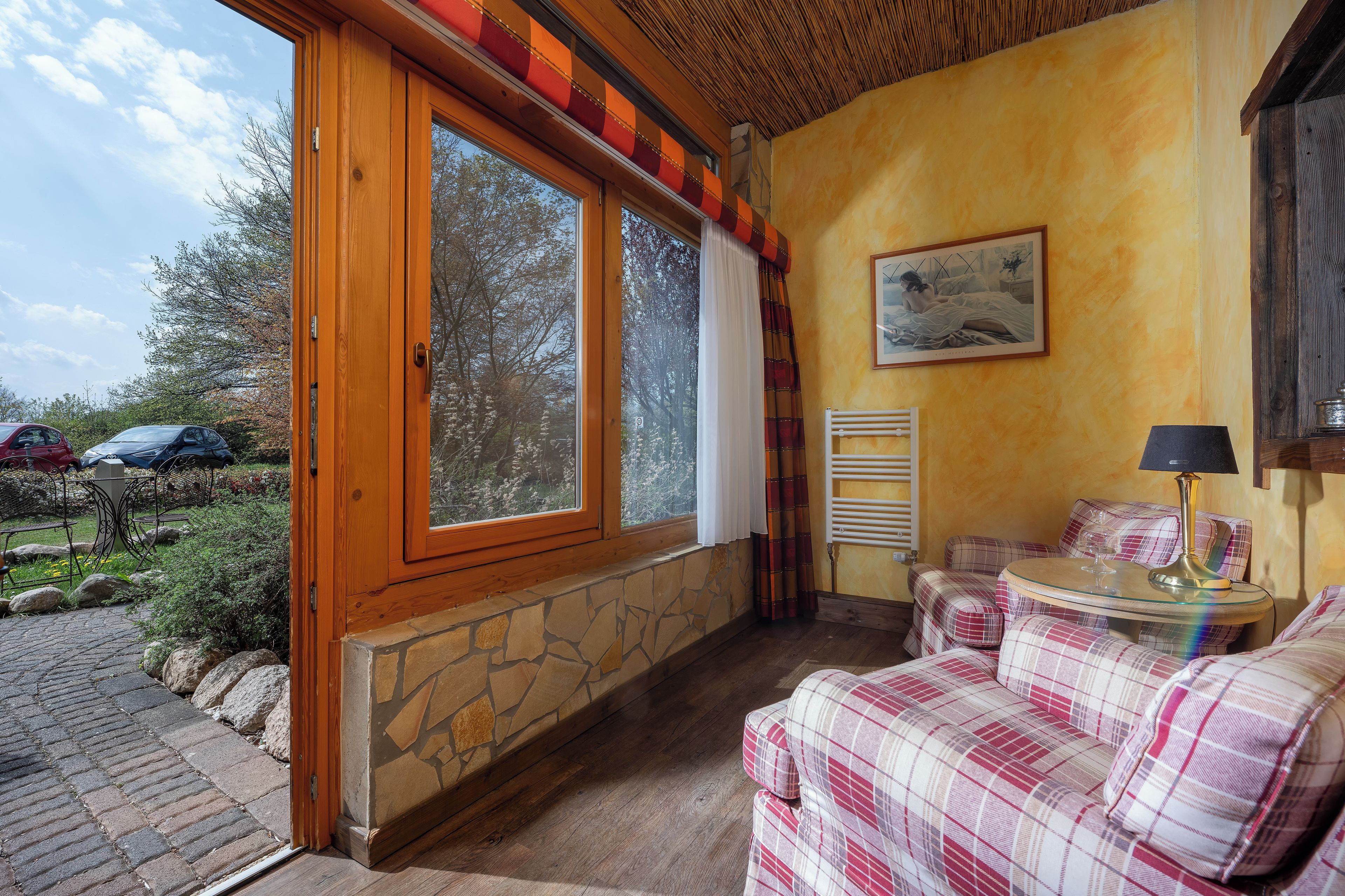 A cozy room with a large window, a painting, a plaid sofa, and a table with a lamp.