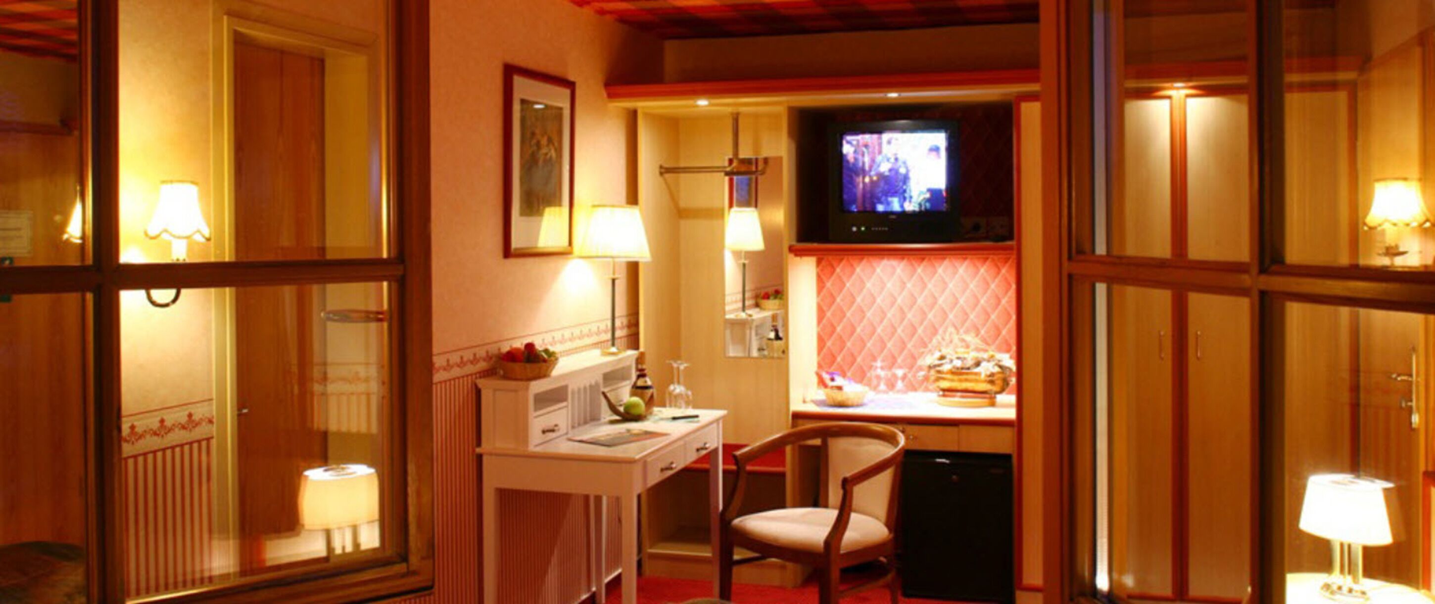 Una habitación de hotel acogedora con televisión, escritorio con lámpara, una silla y una pequeña zona de kitchenette.