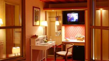 Una habitación de hotel acogedora con televisión, escritorio con lámpara, una silla y una pequeña zona de kitchenette.