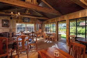 Un comedor rústico con mobiliario de madera, ventanas amplias y un techo con vigas a la vista.