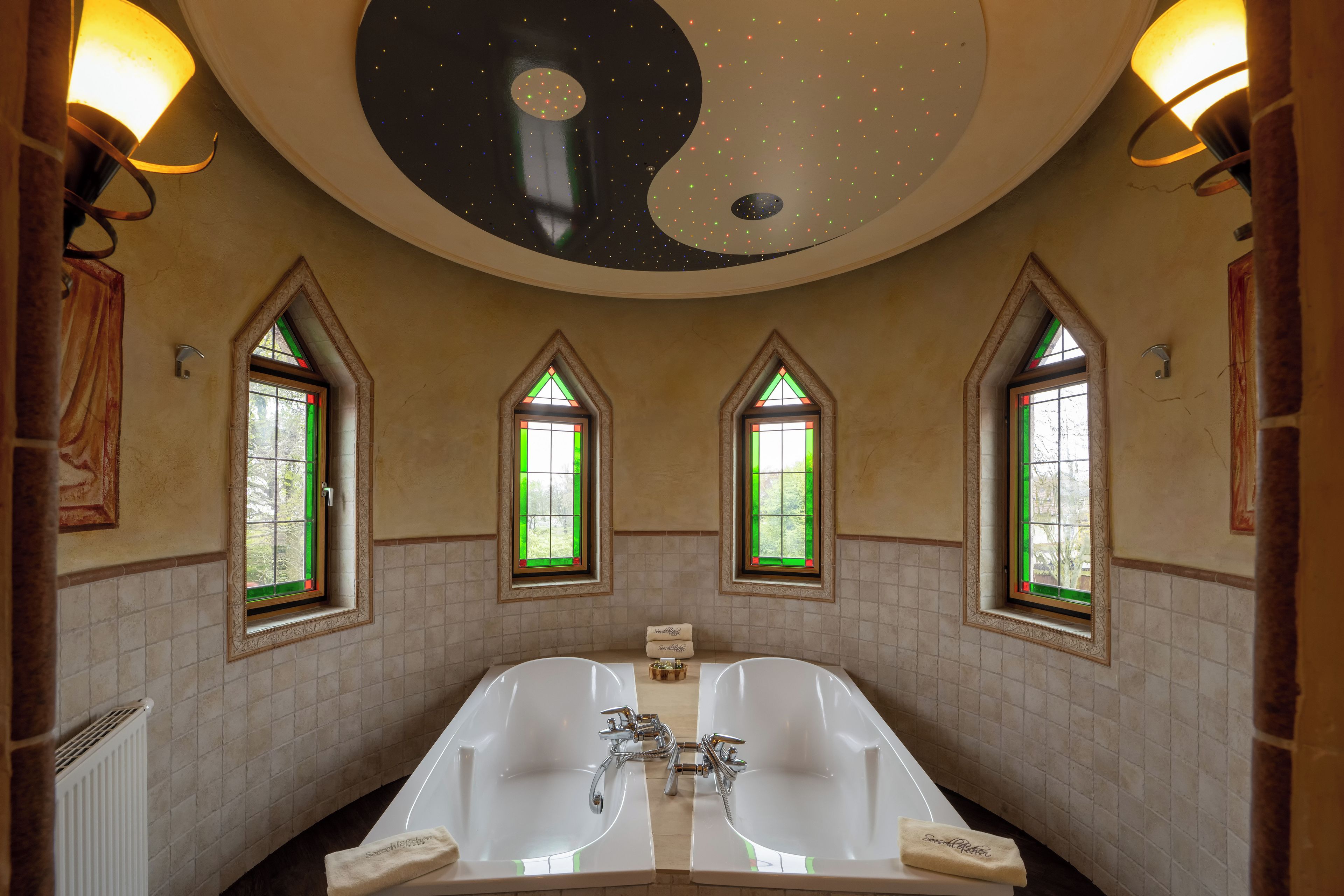 A bathroom with a large bathtub, two windows with green-tinted glass, and a ceiling with a starry design.