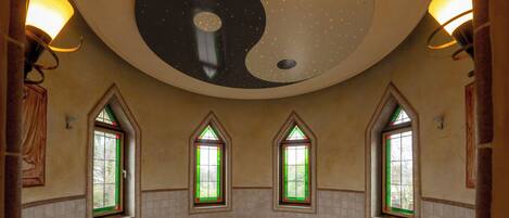 A bathroom with a large bathtub, two windows with green-tinted glass, and a ceiling with a starry design.