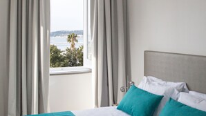 Habitación de hotel con cama, cortinas y vista al mar.