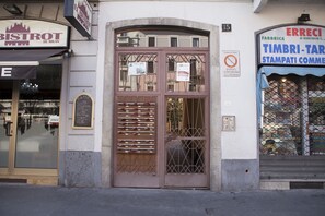 Un edificio con una puerta marrón, un cartel que dice 'BISTROT DE MILAN' a la izquierda y otro cartel que dice 'ERRECI FABBRICA TIMBRI-TAR' a la derecha.