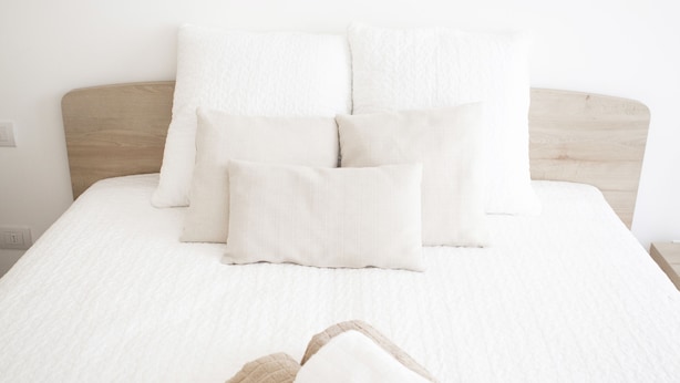 Una cama bien hecha con ropa blanca y una toalla marrón encima.