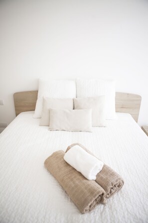 Una cama bien hecha con ropa blanca y una toalla marrón encima.