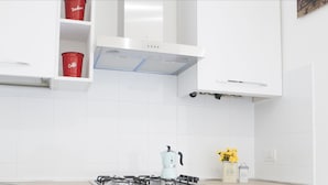 Una cocina moderna con armarios blancos, una estufa a gas y una taza roja en la repisa.